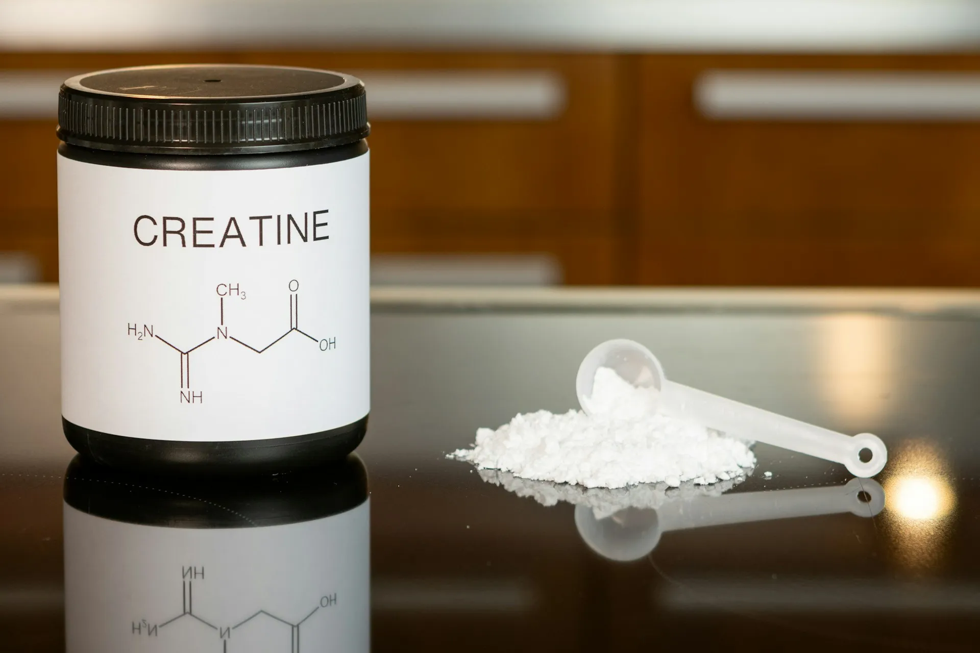 Bottle of creatine monohydrate powder next to a spoon on a table