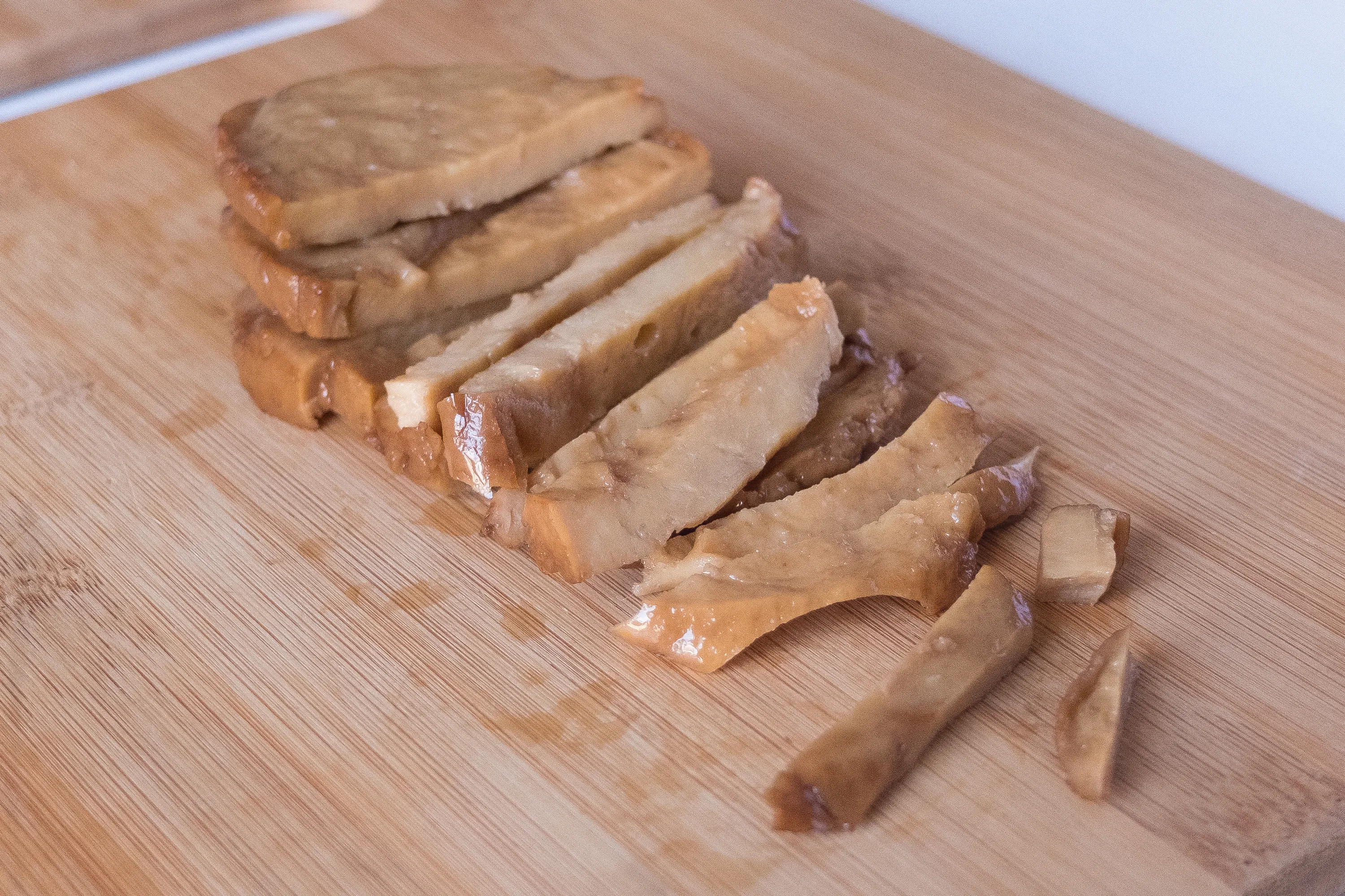 Three slices of seitan on a cutting board, half chopped into smaller pieces